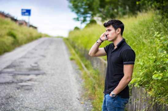 Young man on side of a road, calling and waiting for taxi